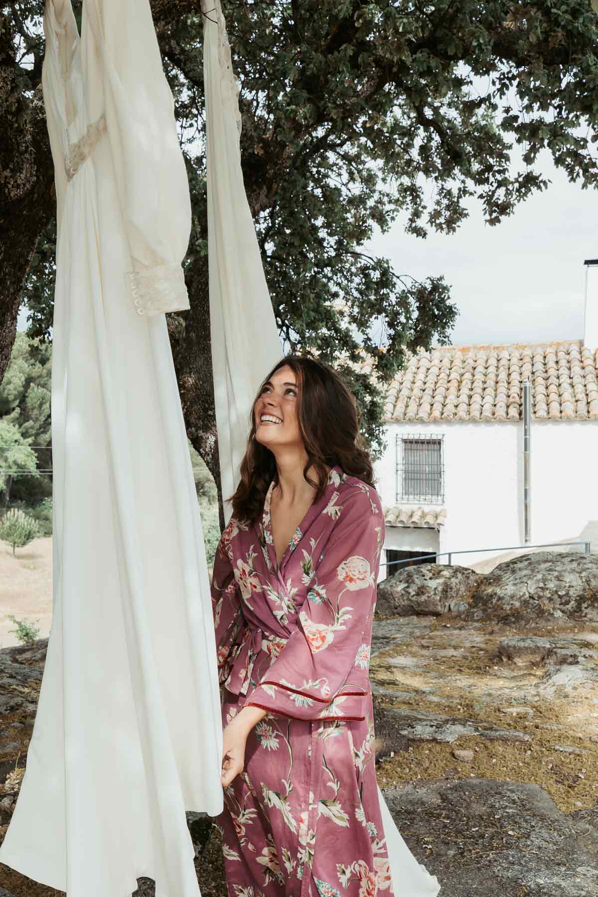Novia en bata rosa contemplando su vestido entre olivos en Andújar, Jaen