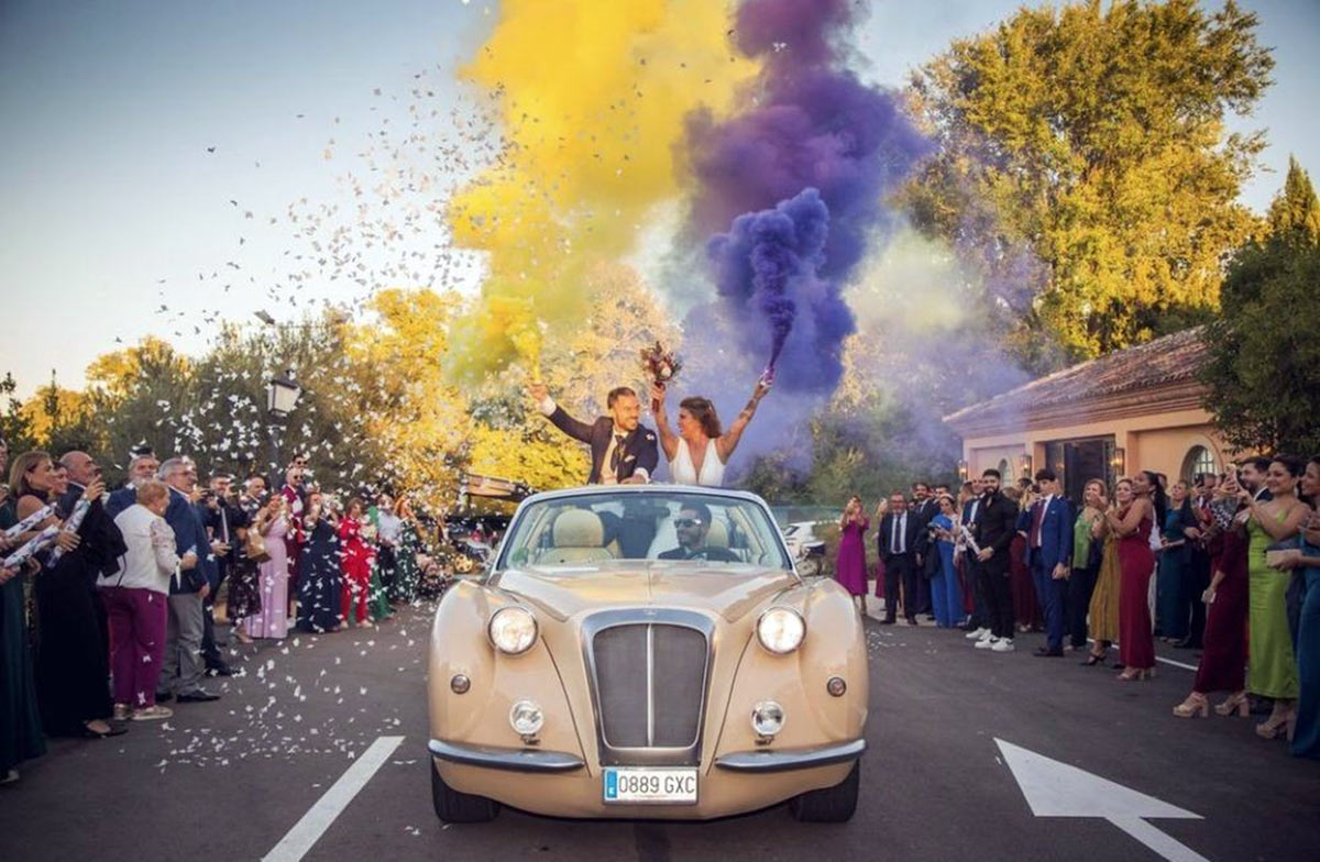 Novios en el coche clásico con bombas de humo de colores